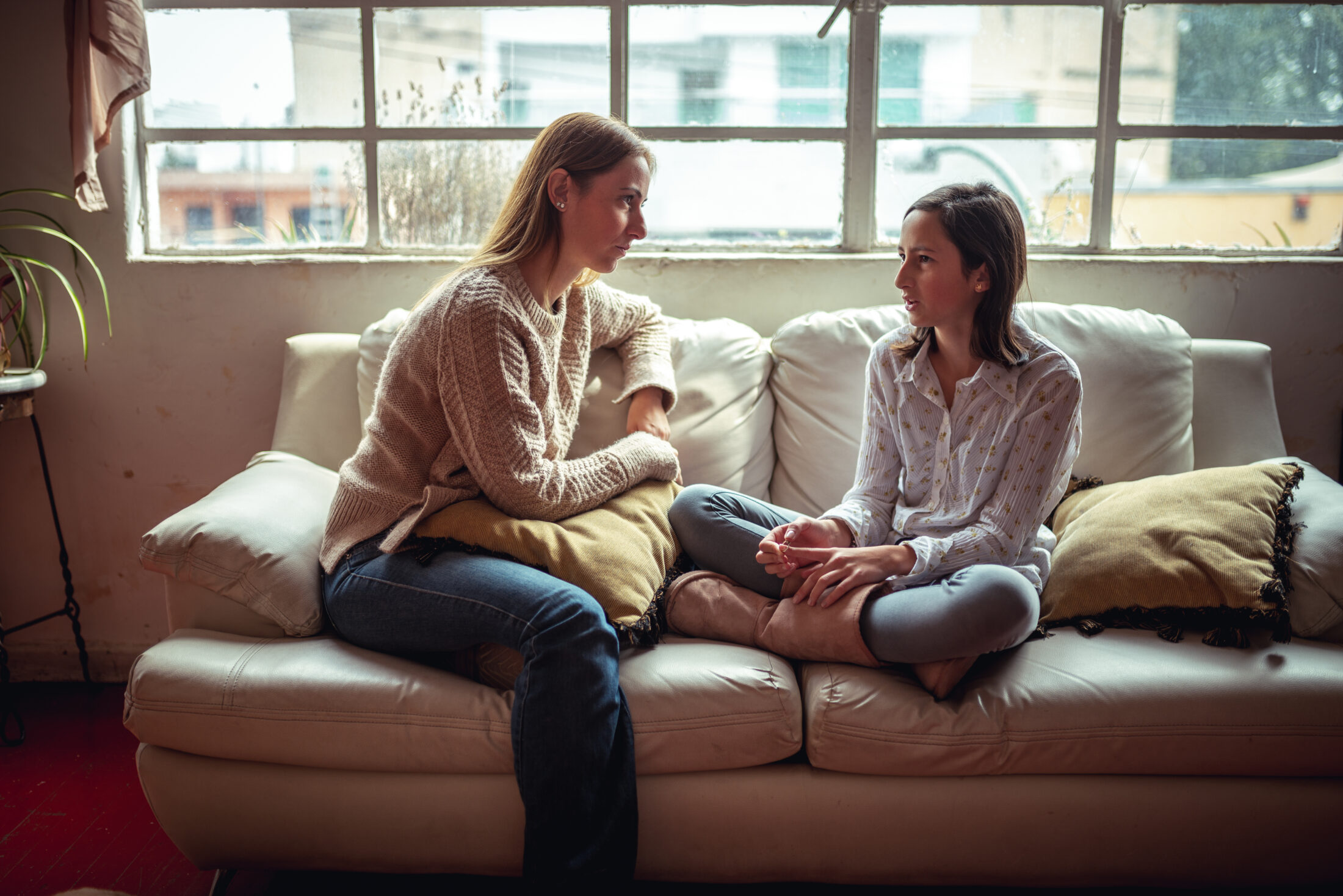 Mother is talking to daughter on sofa.