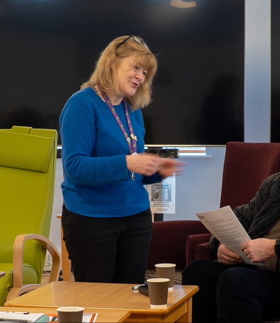 Female wearing a lanyard talking to seated people
